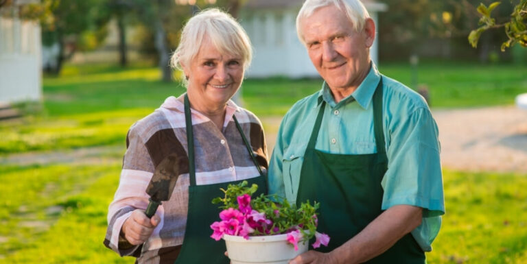 Elderly Couple Holding Flowers and Garden Tools Outdoors at an Independent Living Facility